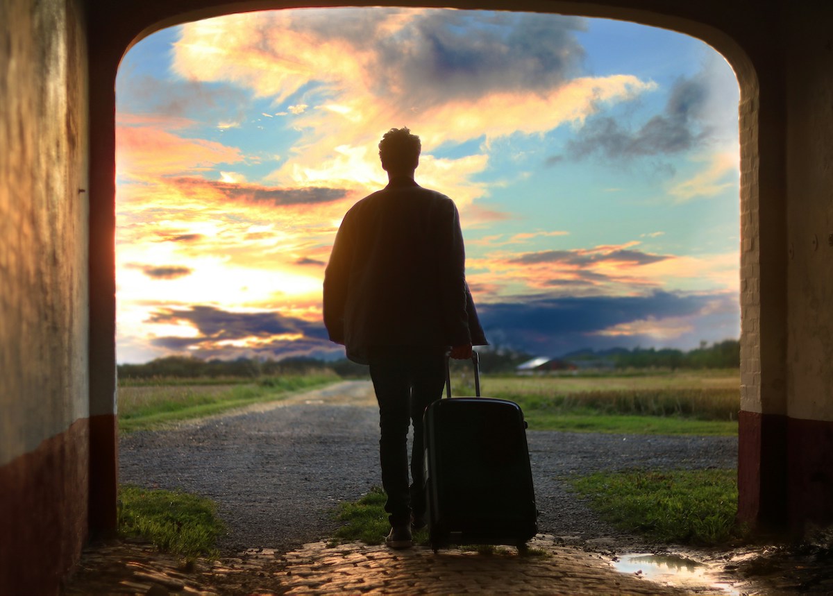 A man walking into the sunset with a suitcase