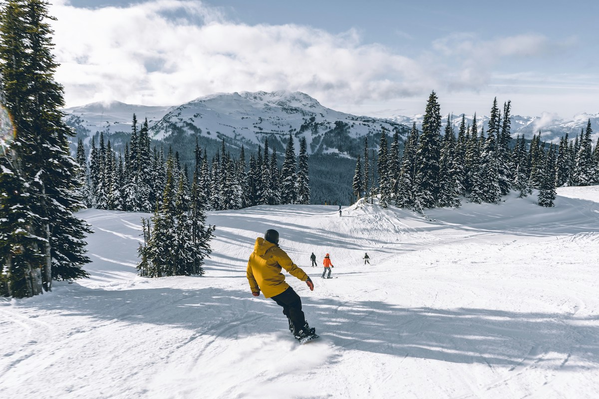 A man riding down Whistler slope on a snowboard